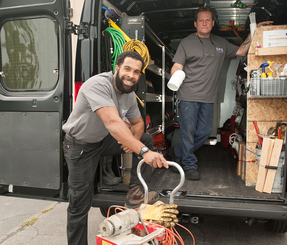 Photograph of two Rochester plumbers standing in a service truck