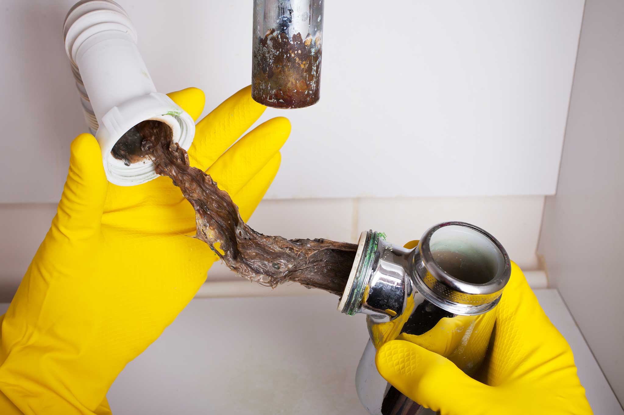 Yellow-gloved hands pull apart plumbing showing clump of wet hair
