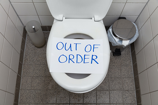 Top-down photo of clogged toilet with white paper reading “Out of Order” on the seat